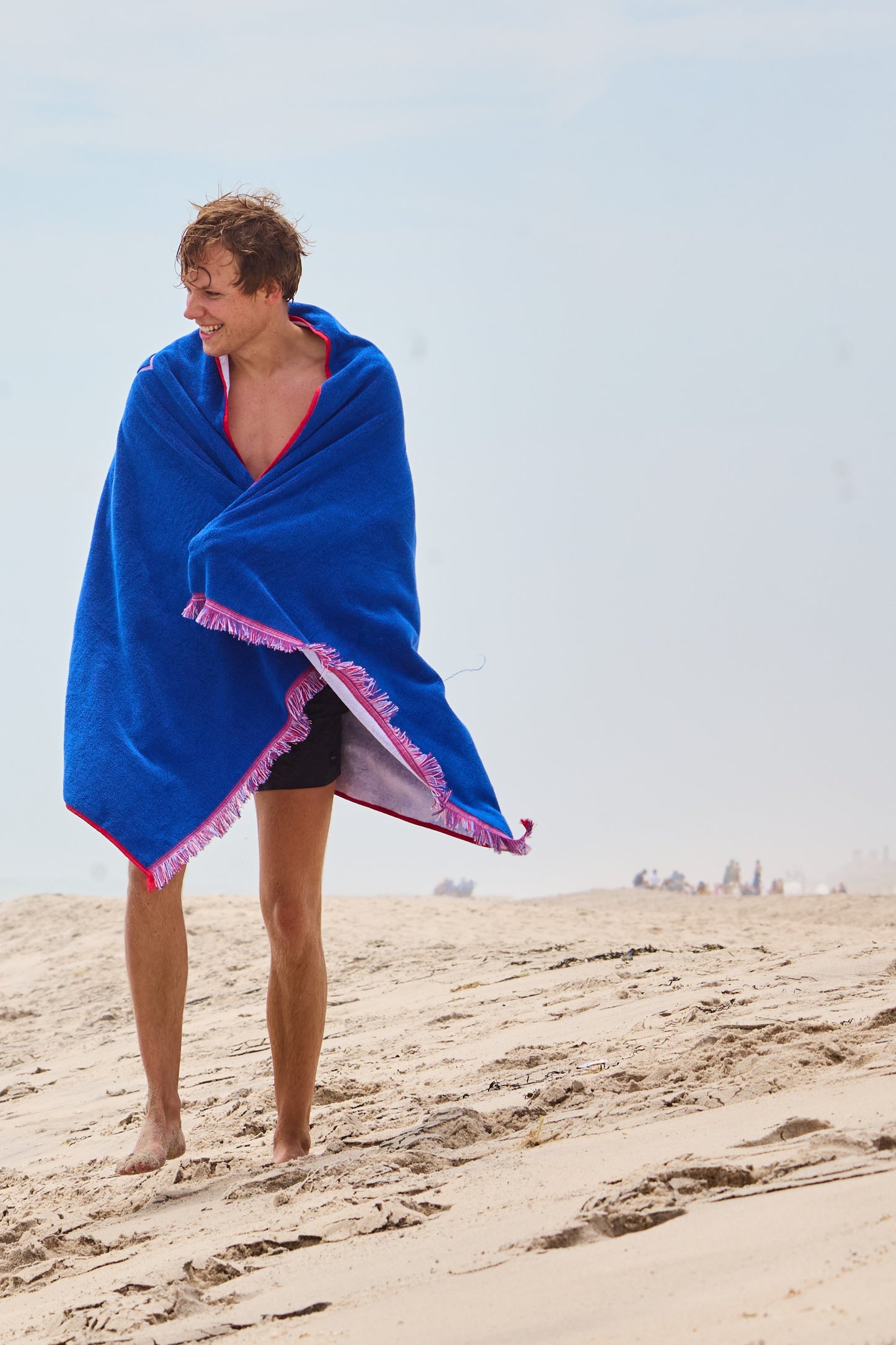 Man smiling and walking at the beach wrapped in his terrycloth beach board after swimming in the ocean