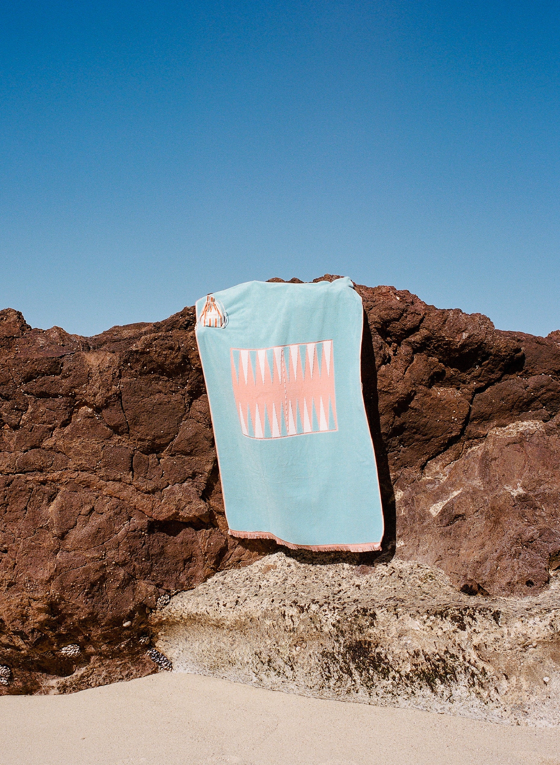 Photo of the orange and blue Beach Board hanging from a rock