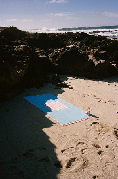 Artistic photo of blue and orange beach board on a rocky beach with a wave in the background